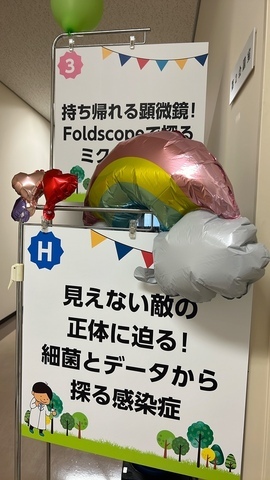 入口の看板「見えない敵の正体に迫る！　細菌とデータから探る感染症」「持ち帰れる顕微鏡！ Foldscopeで探るミクロの世界